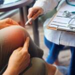 A clinician examining a patient knee while making notes