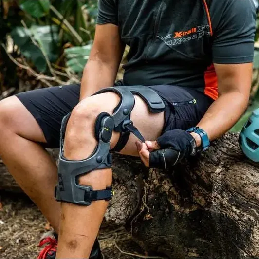 Cyclist fitting a knee brace while sitting on a log