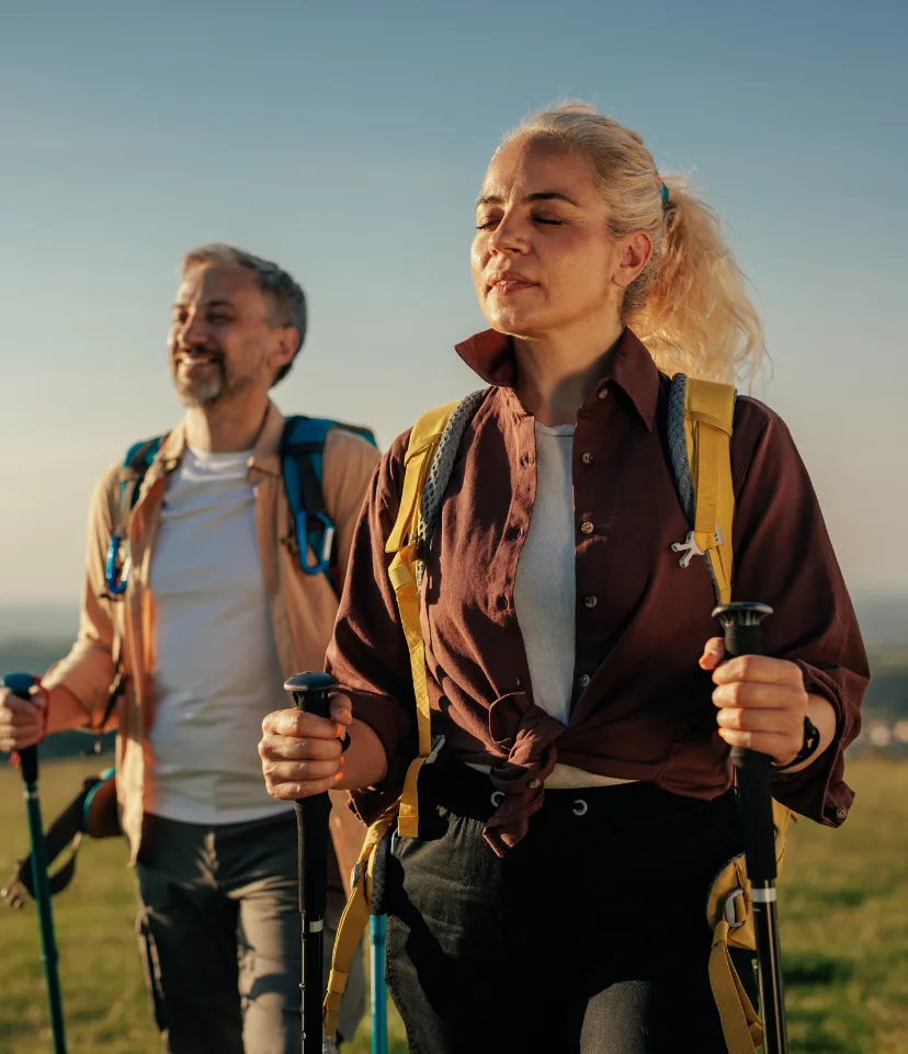 Man and woman walking with trekking poles in evening sun